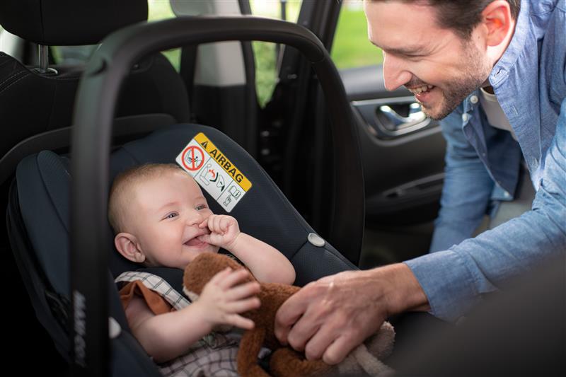 A man putting a small child into a car seat.